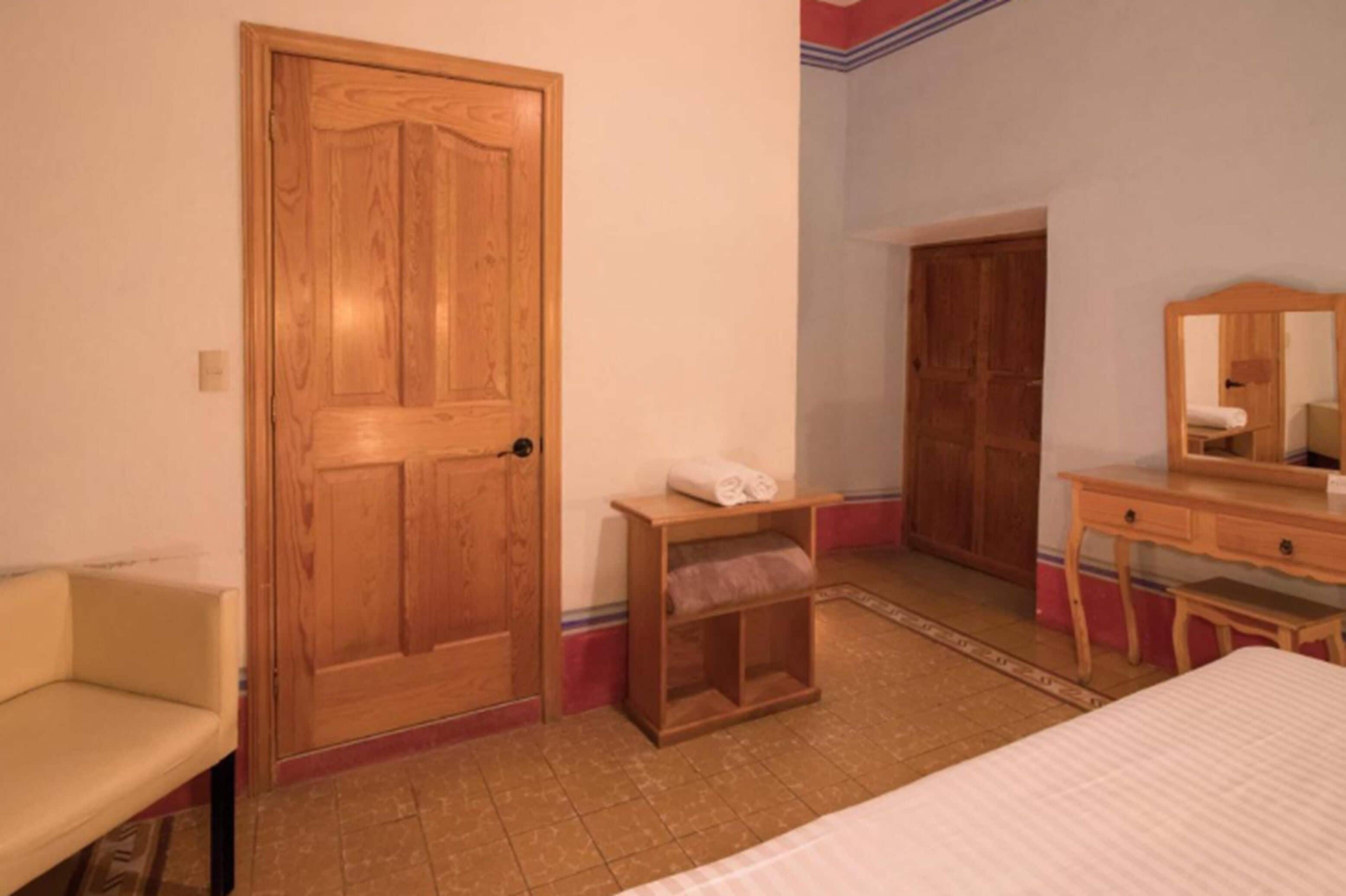 Un dormitorio con puerta de madera, una cama, cómoda de madera y un espejo.