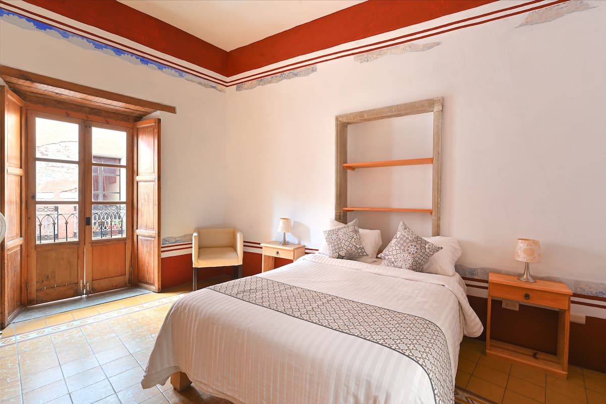 Une chambre à coucher avec un grand lit, une chaise, une table de chevet et une fenêtre.