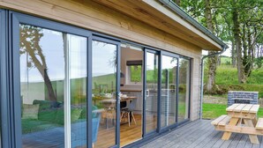 Una casa moderna con ampie porte scorrevoli in vetro, un patio in legno e un’area barbecue.