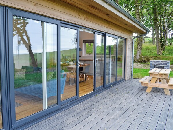 Una casa moderna con grandes puertas de cristal correderas, una terraza de madera y una zona de barbacoa.