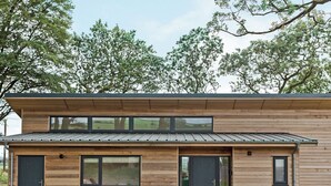 Una moderna casa a due piani in legno, con ampie finestre, una porta d'ingresso scura e un piccolo portico.