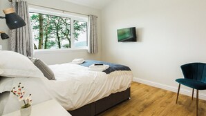 Una camera da letto con un letto, una TV, una sedia, una finestra con tende e una piccola pianta.