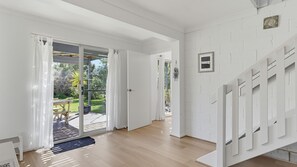 Quarto espaçoso com piso de madeira, porta de vidro deslizante para área externa e escada com corrimão branco.