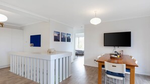 Eine moderne Küche mit einer zentralen Kochinsel, einem Essbereich mit Holztisch und -stühlen sowie einem an der Wand montierten Fernseher.