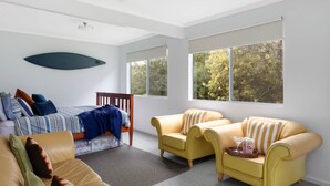 Ein Schlafzimmer mit einem Bett, zwei gelben Sesseln, einer Couch, einem großen Fenster und einem Deckenventilator.