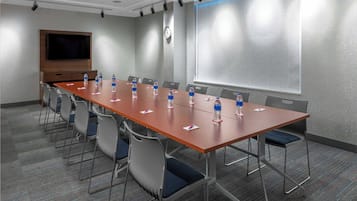 A conference room with a long table, chairs, water bottles, a clock, and a projector screen.