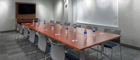 A conference room with a long table, chairs, water bottles, a clock, and a projector screen.