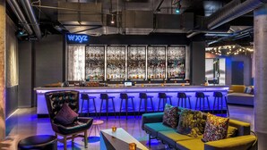 A bar area with a neon sign, bar stools, and a seating area with a sofa and ottomans. - Aloft by Marriott Denver North Westminster (Westminster)