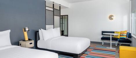 Una habitación de hotel moderna con dos camas, un sofá, una pequeña mesa y un tapete a rayas de colores.