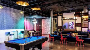 A pool table in a modern lounge area with red chairs, a bar, and a seating area with a large screen. - Aloft by Marriott Denver North Westminster (Westminster)
