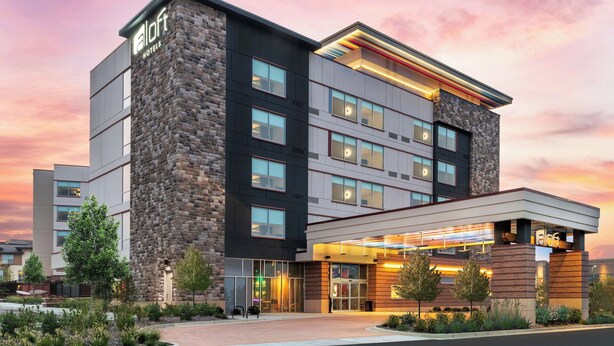 A modern hotel building with a stone facade, multiple floors, and a well-lit entrance. - Aloft by Marriott Denver North Westminster (Westminster)