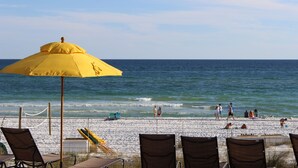 A beachside view with a yellow umbrella, beach chairs, and a railing overlooking the ocean.