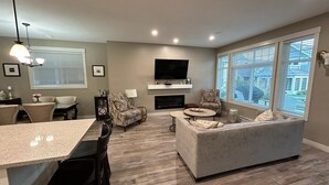 A modern living room with a fireplace, a flat-screen TV, and a large window. - OSOYOOS PRIVATE RESORT HOME STEPS FROM THE LAKE (Oliver)