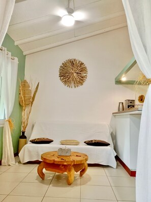 A room with a bed, a wooden stool, a wall decoration, and a ceiling fan.
