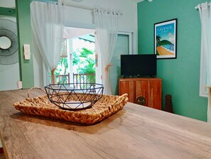 A room with a wooden table, a woven tray, a television on a wooden cabinet, and a framed picture on the wall.