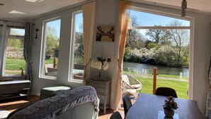 A room with large windows, a dining table, a sofa, and a chair. - River Retreat Lodge is front line with panoramic views over the river Avon. (Stratford-upon-Avon)
