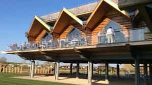 A modern building with a wooden exterior and a covered outdoor area with seating. - River Retreat Lodge is front line with panoramic views over the river Avon. (Stratford-upon-Avon)