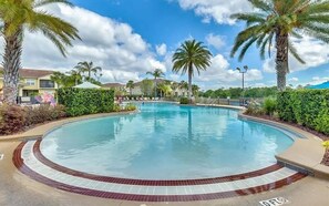 Una piscina con borde de azulejos, rodeada de palmeras y un cielo despejado.