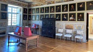 Une pièce avec un plancher en bois, une table à cadre rouge, un meuble noir et un mur orné de portraits encadrés.