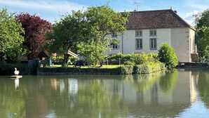 Un bâtiment à la façade blanche et au toit brun, situé au bord d’une étendue d’eau calme.