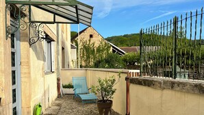 Une terrasse avec une table, un pot de fleurs, une chaise bleue et un mur en pierre.