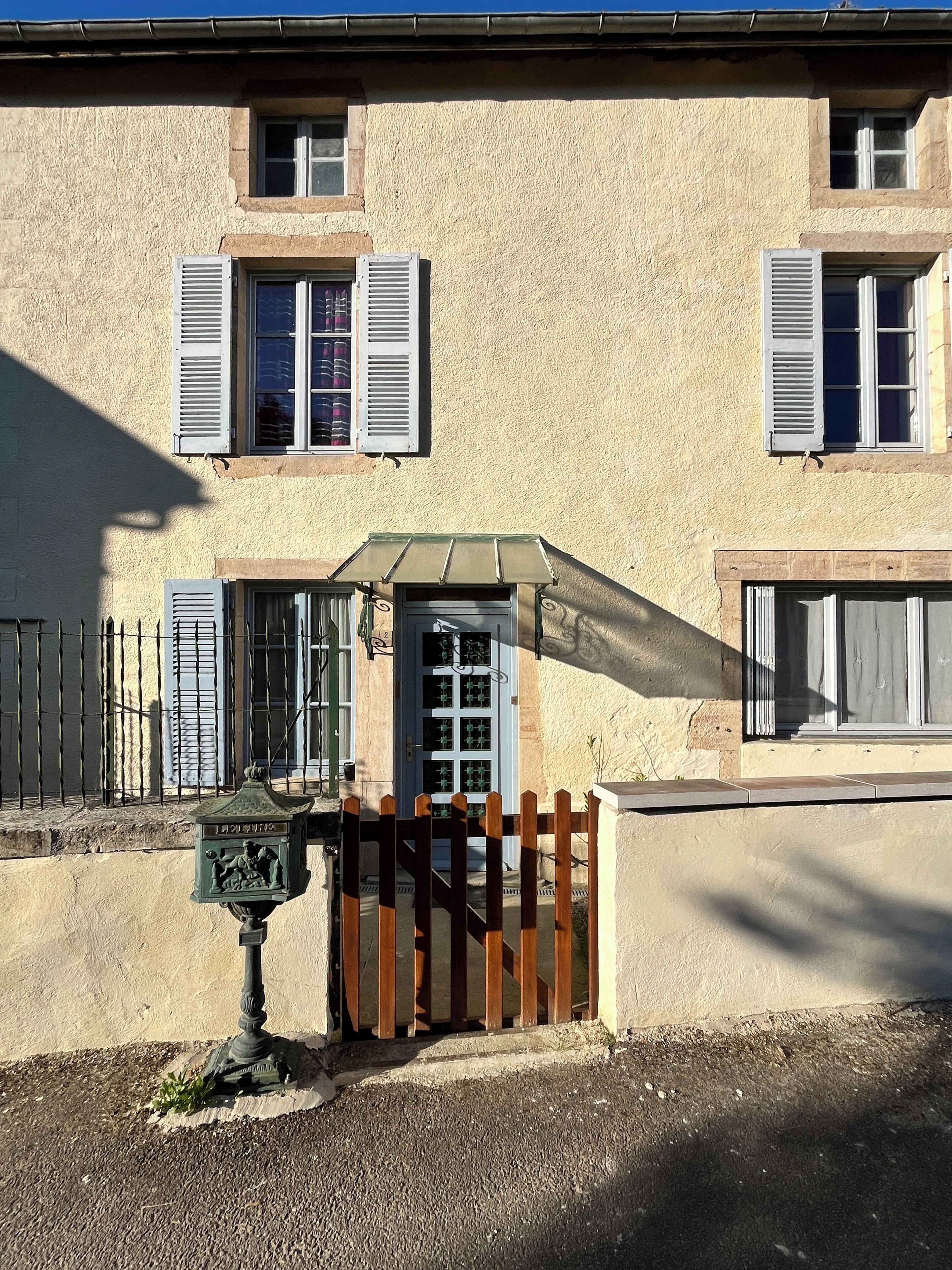 A building with a textured facade, a gated entrance, and a small porch with a green awning.