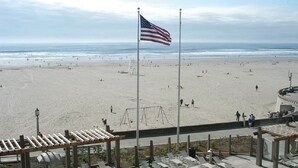 Une plage avec un drapeau américain, une aire de jeux et une promenade en bord de mer dotée de bancs.