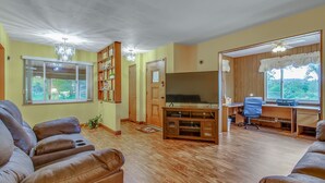 Un salon équipé d’un téléviseur à écran plat, de canapés en cuir, d’un plancher en bois, d’une bibliothèque et d’un bureau avec une chaise.