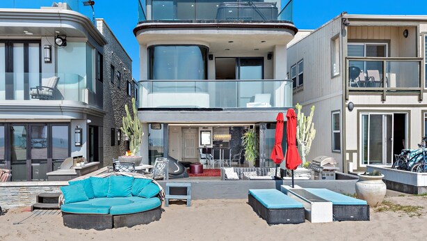 Una moderna casa a due piani con un balcone, un'area salotto esterna e un patio con barbecue.