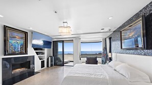 Una camera da letto moderna con un ampio letto, un caminetto, una TV e un balcone con vista sul mare.