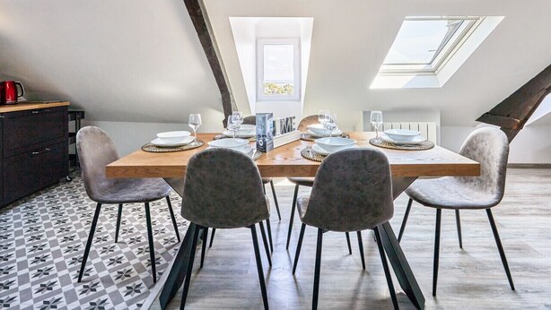 Un coin repas avec une table en bois, quatre chaises et un petit meuble. Des lucarnes se trouvent au-dessus de la table.