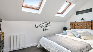 Une chambre avec un lit, deux fenêtres de toit, un radiateur et un panneau décoratif mural.