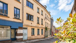 Une vue de rue d'un immeuble doté de nombreuses fenêtres et de balcons, d'une devanture de magasin avec une enseigne, et d'un ciel dégagé.