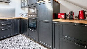 Une cuisine compacte avec des meubles de couleur sombre, un four encastré, un four à micro-ondes et une machine à café.