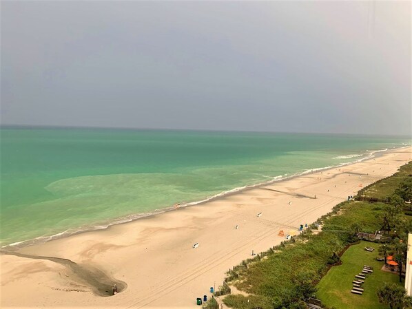 Uma praia com águas turquesa cristalinas, uma orla arenosa e uma fileira de cabanas de praia ao longo da costa.