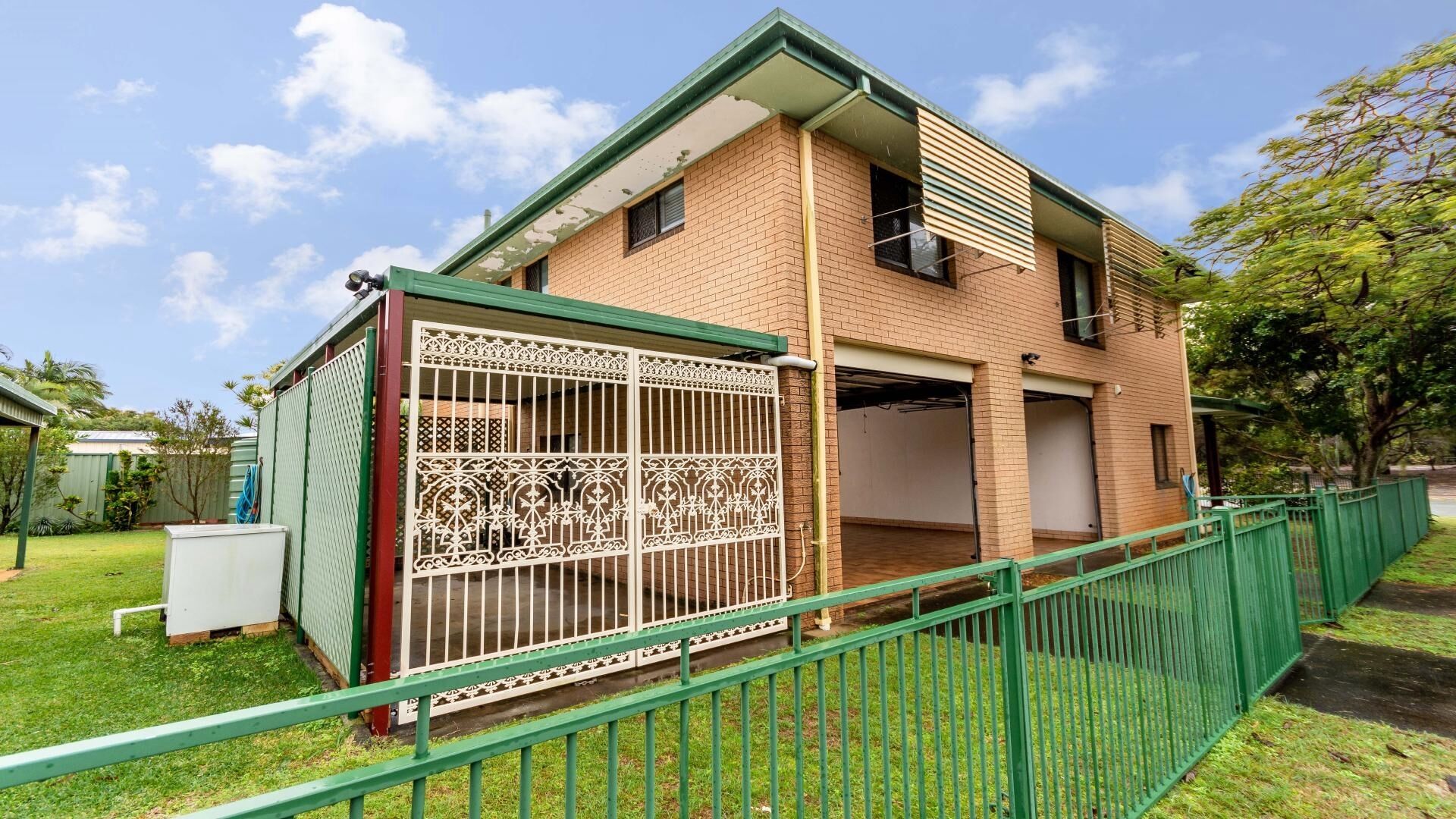 A two-story brick house with a green roof, a fenced yard, and a garage.