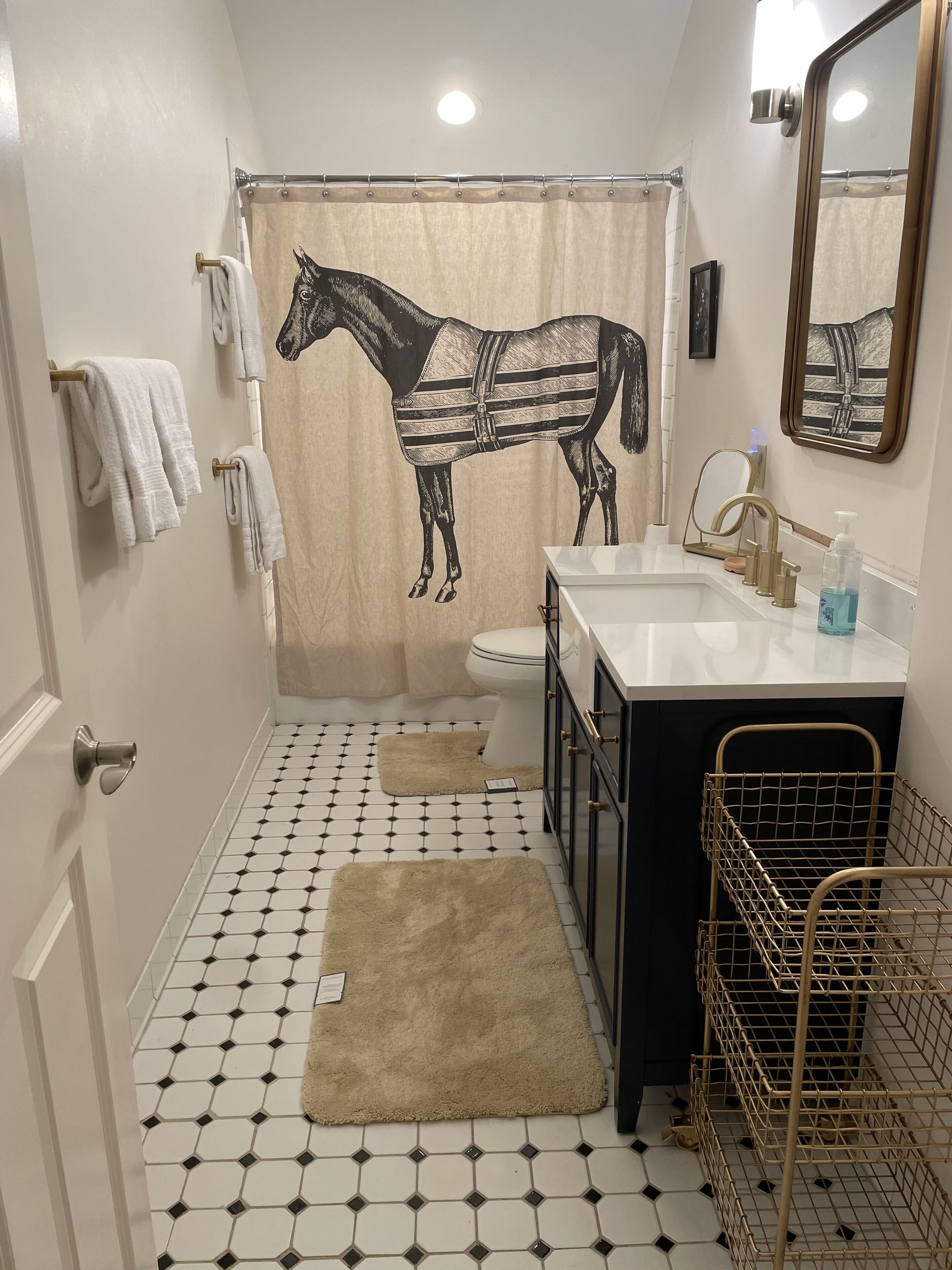 A bathroom with a horse-themed shower curtain, a toilet, a sink with a mirror, and a towel rack.