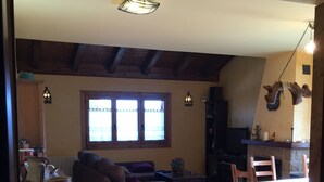 A cozy living room with a fireplace, a sofa, a dining table with chairs, and a large window with curtains.