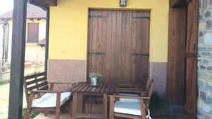 An outdoor patio with a wooden table and chairs, a potted plant, and a stone wall.