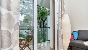 Een kamer met een schuifdeur naar een balkon, een bank met kussens en een vloerlamp.