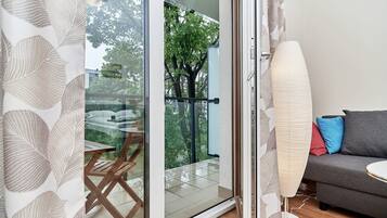 Ein Zimmer mit einer Schiebetür zum Balkon, einer Couch mit Kissen und einer Stehlampe.