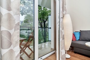 A room with a sliding glass door leading to a balcony, a sofa with cushions, and a floor lamp.