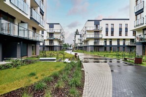 A modern residential building with balconies, a paved walkway, and a grassy area.