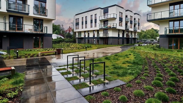 Een modern woongebouw met meerdere balkons, een verhard looppad en een aangelegde tuin.