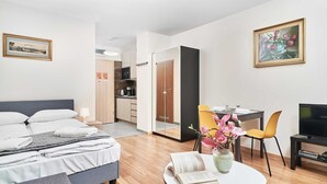 Een moderne hotelkamer met een bed, nachtkastje, een rond tafel met een boek en bloemen, een televisie en een zithoek met stoelen.