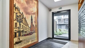 Un couloir orné d’un grand tableau encadré représentant un paysage urbain européen, une porte donnant sur l’extérieur et un coffre-fort fixé au mur.