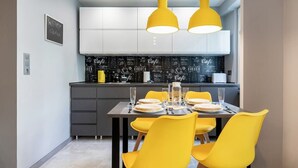 A modern kitchen with white cabinets, a black backsplash with coffee-related text, and yellow pendant lights.