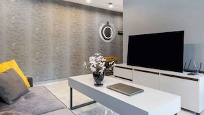 A modern living room with a grey sofa, a white coffee table with a vase and flowers, a flat-screen TV, and a minimalist design.