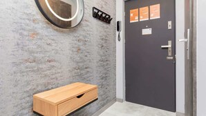 A modern bathroom with a wooden vanity, a round mirror with lights, a dark door with informational cards, and a textured wall.