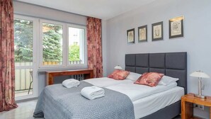 A modern bedroom with a large bed, a wooden nightstand, and a window with curtains.